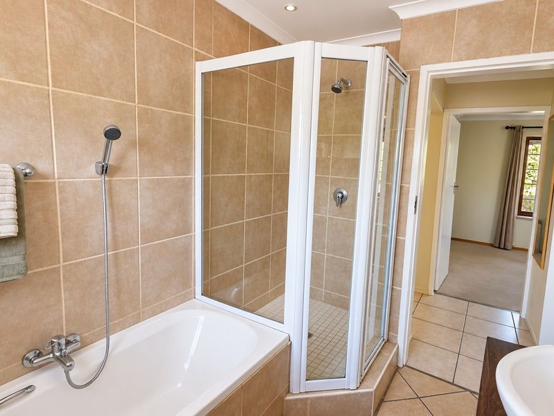 A functional bathroom featuring a separate shower enclosure, bathtub with handheld shower head, and neutral wall and floor tiling.