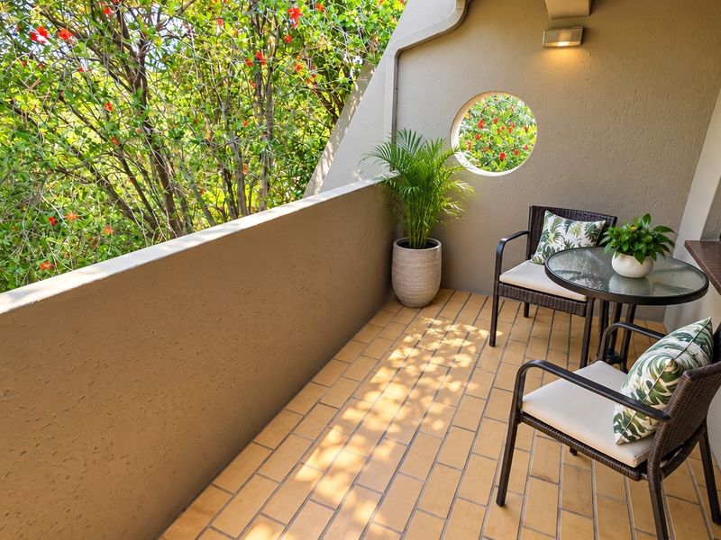 A well-maintained balcony featuring tiled flooring, a unique circular window, and a solid masonry balustrade overlooking lush greenery.