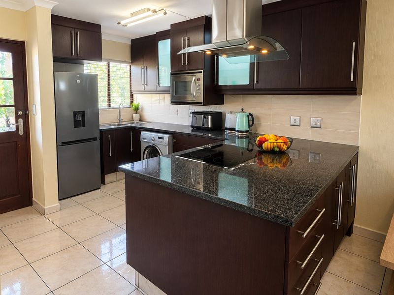 Modern kitchen featuring dark wood cabinetry, granite countertops, stainless steel appliances, and tiled flooring with direct access to the exterior.