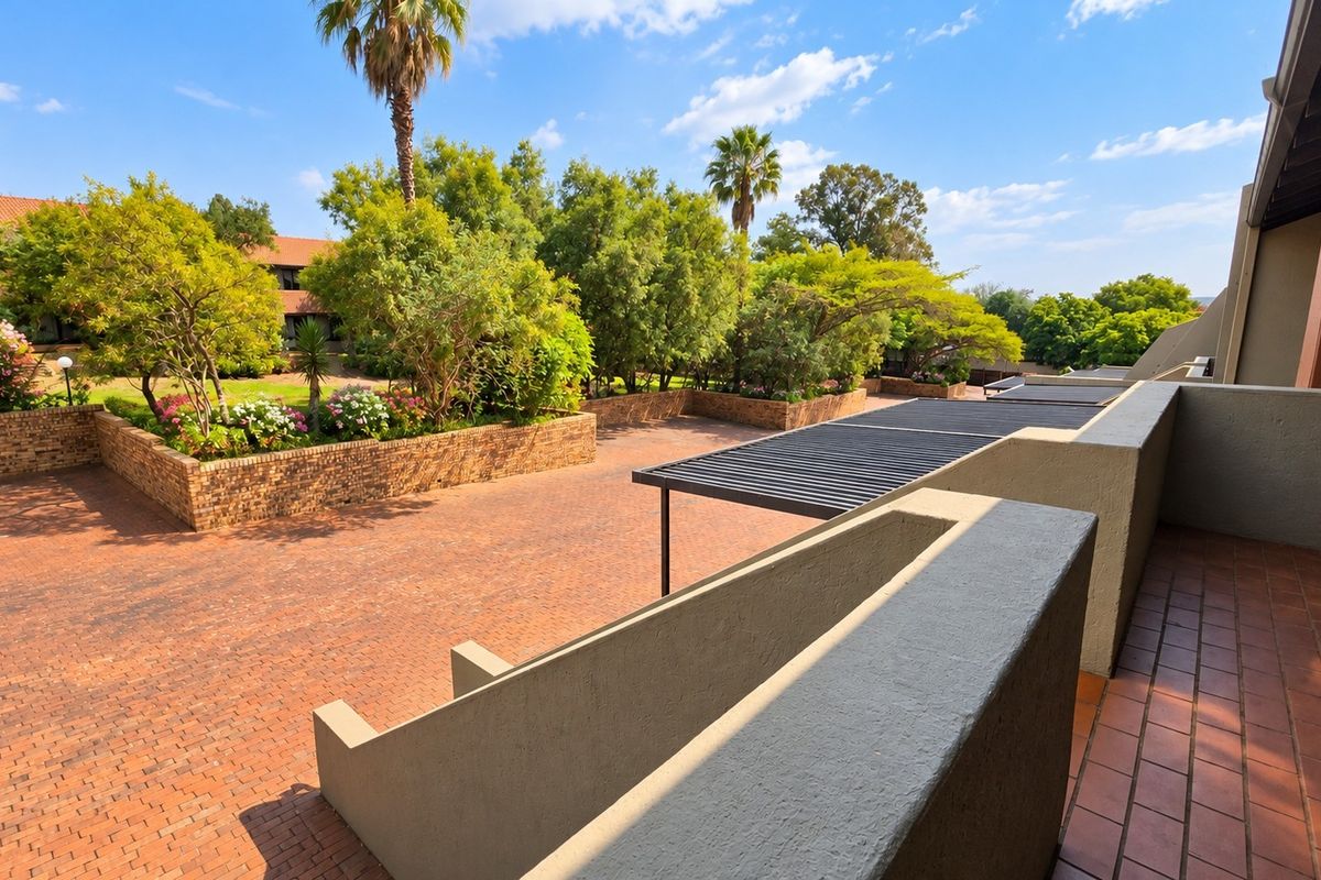 A well-maintained rear courtyard area featuring brick paving, raised garden beds, and a covered balcony space with a metal pergola.