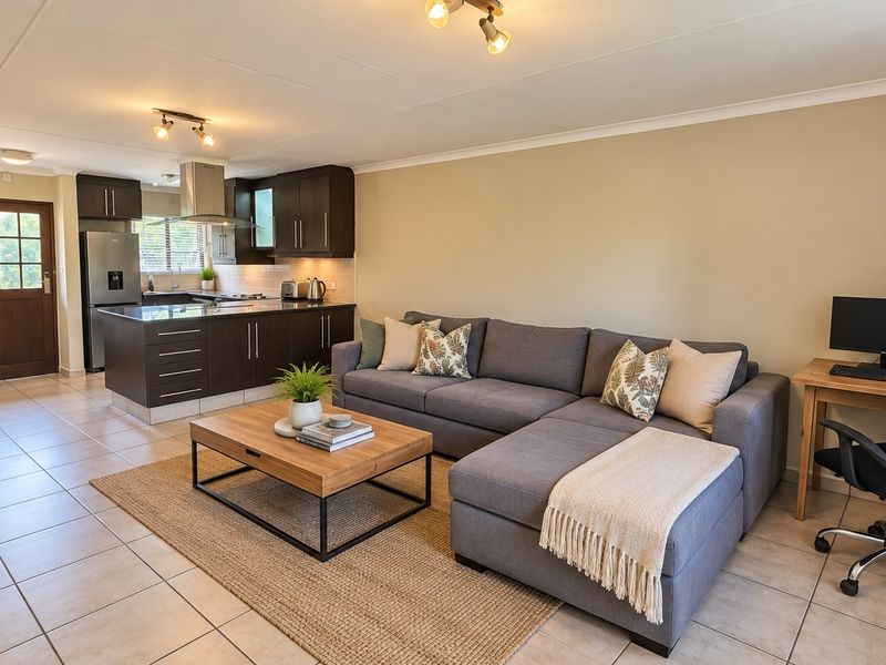 An open-plan living area featuring a modern kitchen with dark cabinetry and tiled flooring, seamlessly flowing into a comfortable lounge space.
