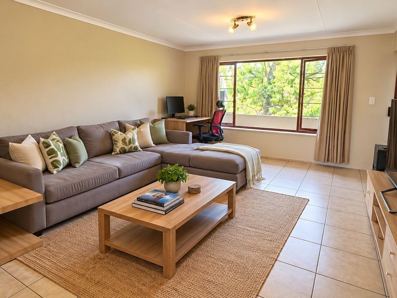 A bright and spacious living room featuring neutral tiled flooring, large windows allowing natural light, and a clean, well-maintained interior finish.