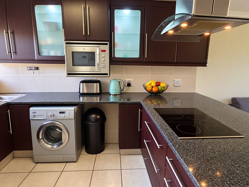 Modern kitchen featuring dark wood cabinetry, granite countertops, integrated appliances, and a sleek electric hob, offering a functional and stylish cooking space.
