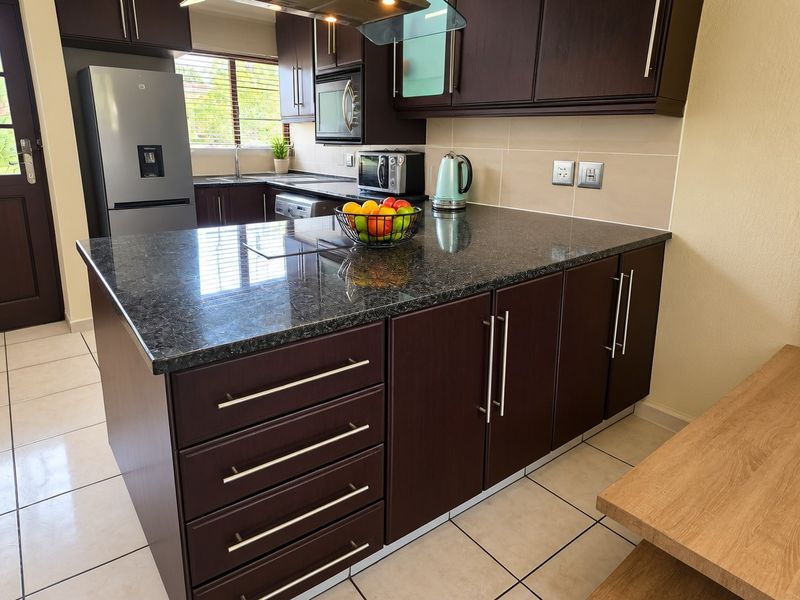 Modern kitchen featuring dark wood cabinetry, granite countertops, a central island, and tiled flooring with a functional layout.