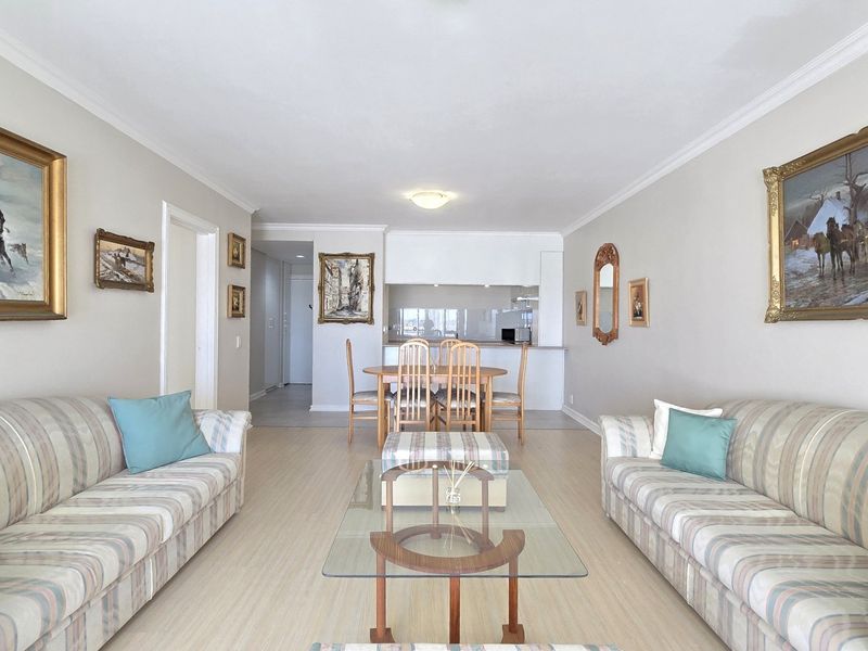 Open-plan living and dining area featuring light laminate flooring, coved ceilings, and a functional kitchen space with built-in cabinetry.