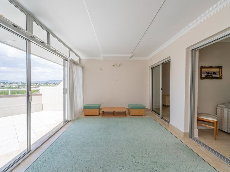 A bright, enclosed balcony area featuring large sliding glass doors, tiled flooring, and access to an outdoor terrace with scenic views.