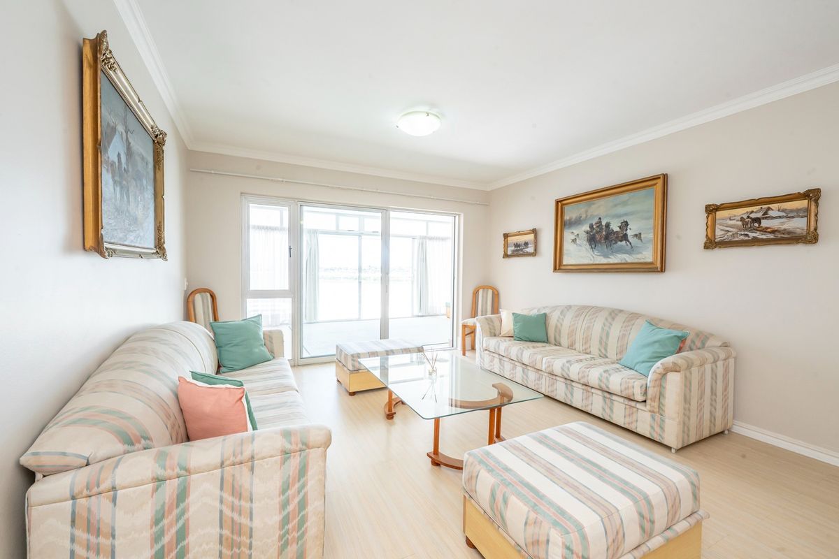 A bright living room featuring light-toned laminate flooring, neutral walls, and a large sliding glass door providing access to the outdoor area.