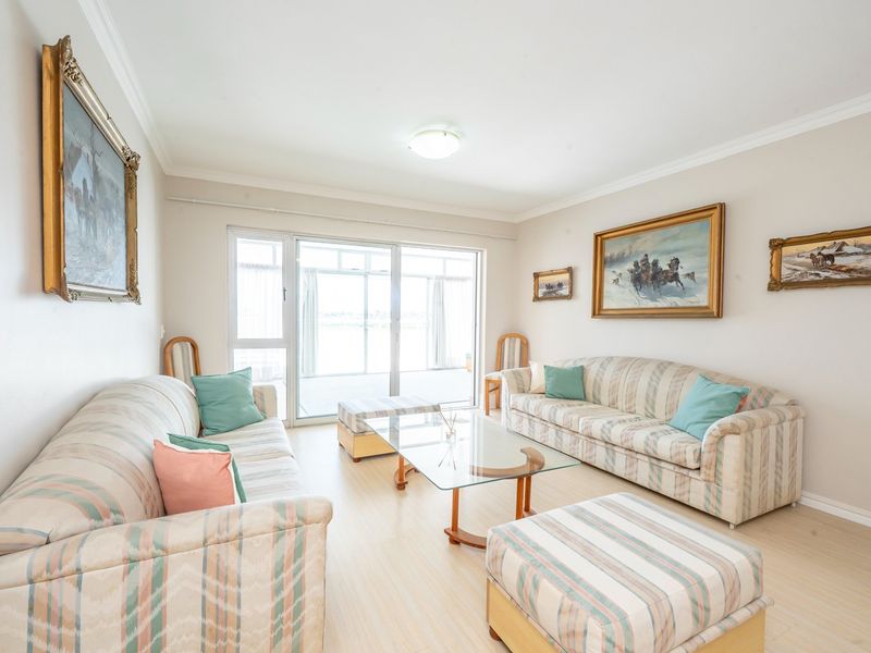A bright living room featuring light-toned laminate flooring, neutral walls, and a large sliding glass door providing access to the outdoor area.