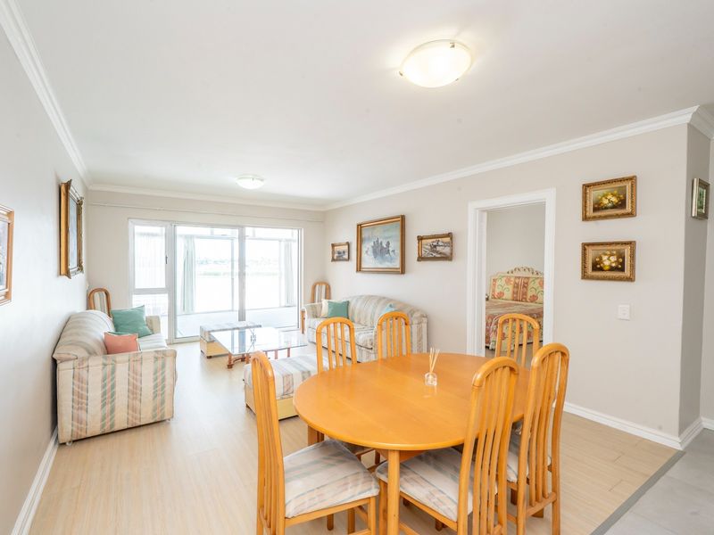 Spacious open-plan living and dining area featuring light laminate flooring, crown molding, and large sliding glass doors leading to an outdoor space.
