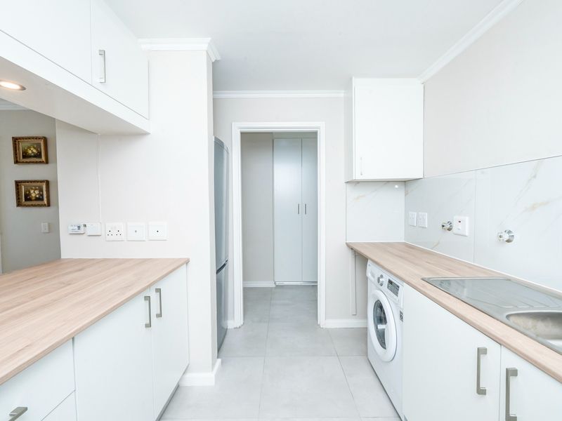 A clean, modern kitchen featuring white cabinetry, light wood-tone countertops, marble-effect splashbacks, and integrated laundry facilities with tiled flooring.