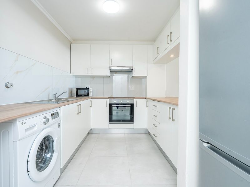 A modern, well-maintained kitchen featuring white cabinetry, light wood-tone countertops, marble-effect splashbacks, and integrated appliances including an oven and extractor fan.