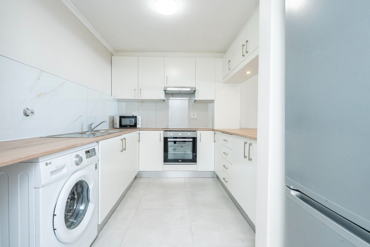 A modern, well-maintained kitchen featuring white cabinetry, light wood-tone countertops, marble-effect splashbacks, and integrated appliances including an oven and extractor fan.
