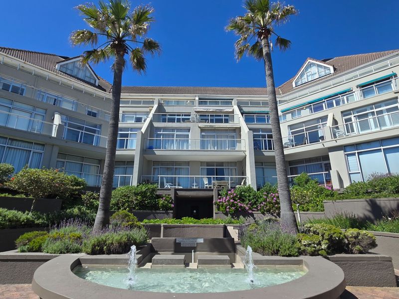 A view of the rear apartment facade featuring tiered balconies, landscaped gardens, and a central water fountain in the courtyard.