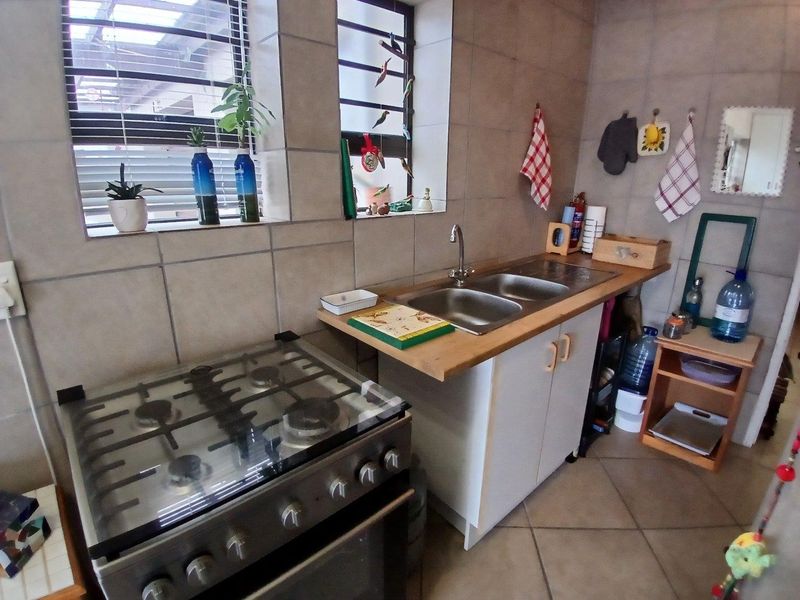 Compact kitchen area featuring a gas stove, double basin sink, tiled splashback, and tiled flooring with natural light from louver windows.
