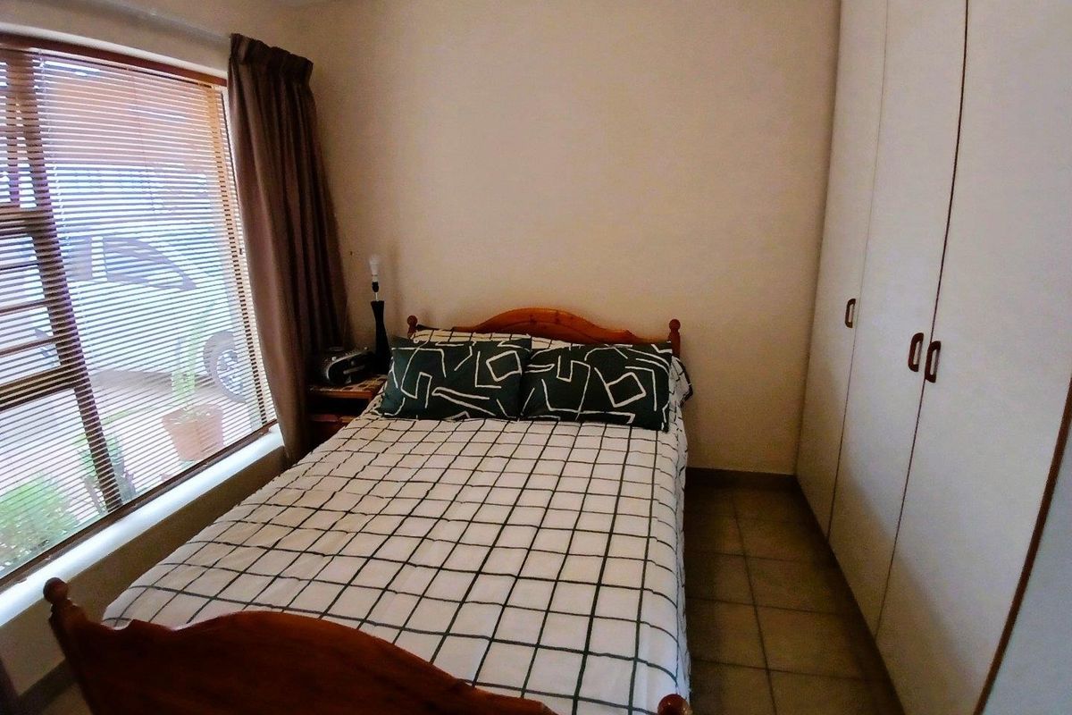 A functional bedroom featuring built-in cupboards, tiled flooring, and a large window providing natural light.
