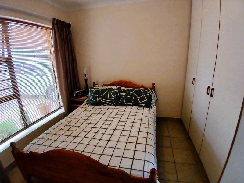 A functional bedroom featuring built-in cupboards, tiled flooring, and a large window providing natural light.