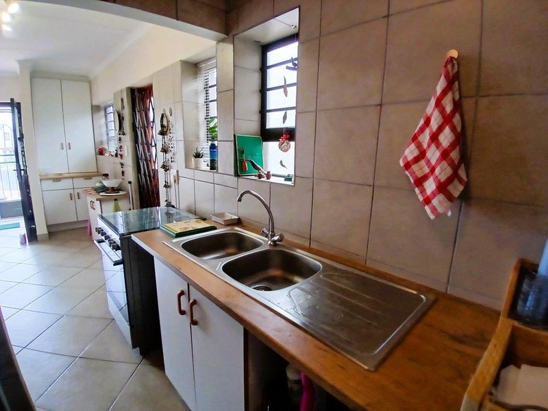 A functional kitchen featuring a double bowl stainless steel sink, tiled splashbacks, and built-in cabinetry with a freestanding stove.