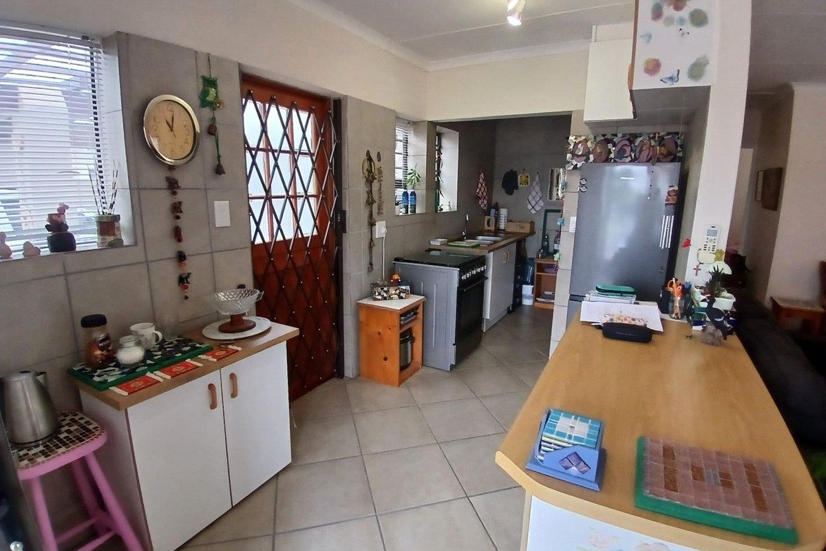 Functional kitchen featuring tiled flooring, built-in cabinetry, a freestanding stove with extractor fan, and a double sink with direct exterior access.