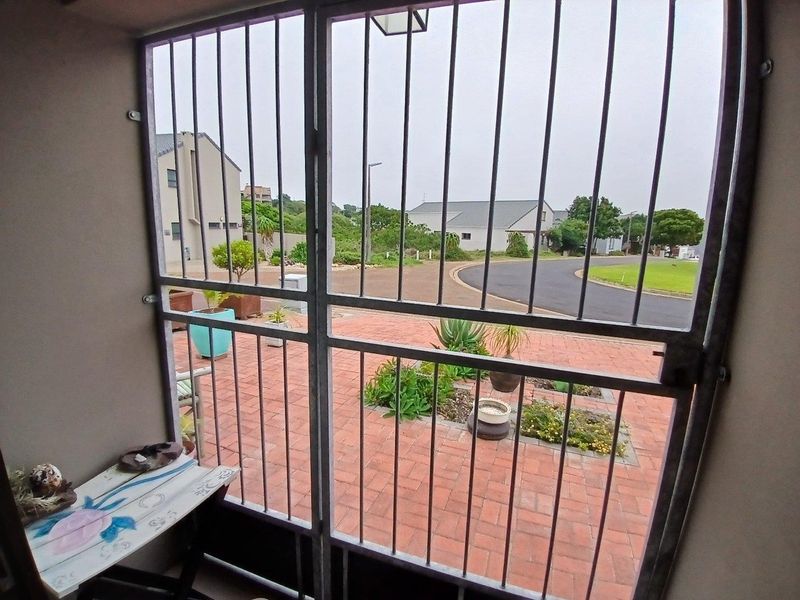 A covered patio area featuring a secure metal gate, overlooking a paved front garden and residential street.