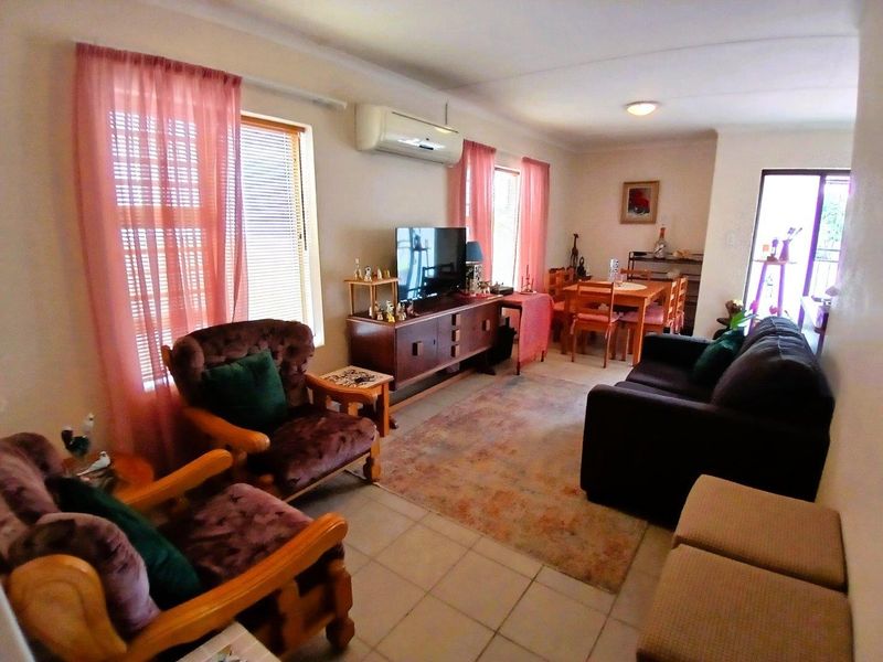 A functional living room featuring tiled flooring, a wall-mounted split-system air conditioner, and access to an outdoor area via a sliding glass door.