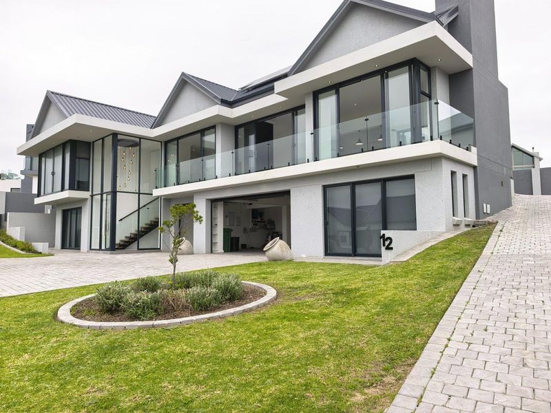 Modern double-story residence featuring contemporary architectural design, glass balustrades, paved driveway, and a well-maintained landscaped garden.