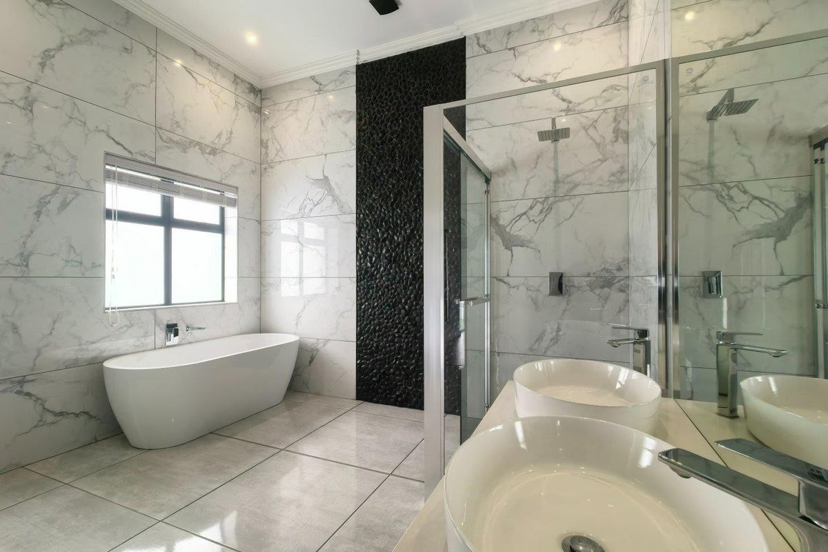 Modern, high-end bathroom featuring a freestanding bathtub, glass-enclosed shower, and dual vessel sinks with elegant marble-look tiling and a striking black feature wall.