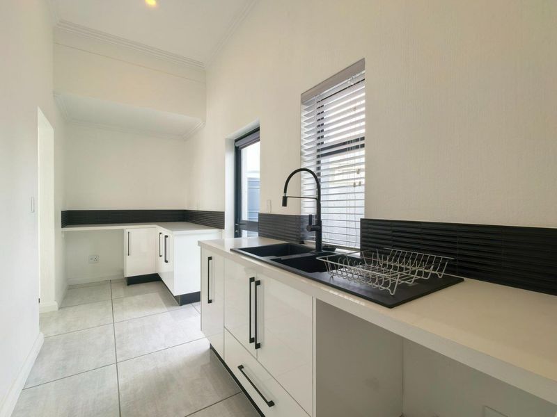 A clean, modern scullery featuring white built-in cabinetry, a black double sink with matching mixer tap, and tiled splashbacks.
