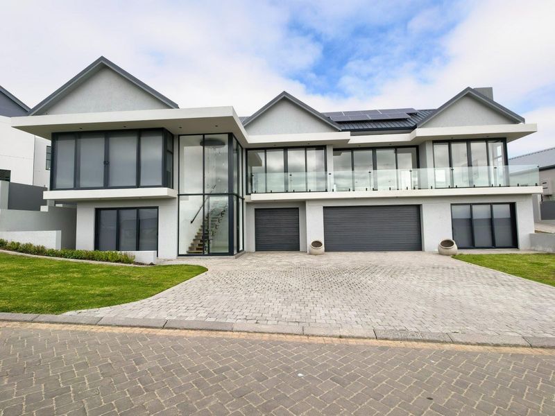 Modern double-story residence featuring a paved driveway, double garage, expansive glass facade, and a balcony with glass balustrades.