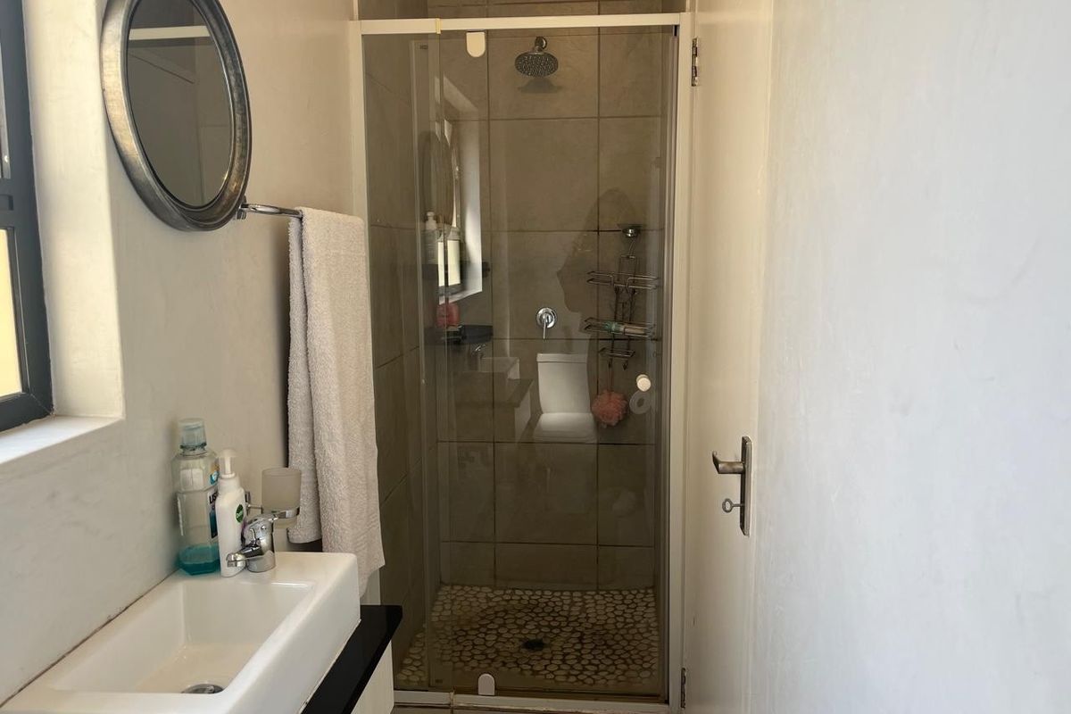 A compact bathroom featuring a tiled shower enclosure with a pebble-style floor and a modern wall-mounted basin.