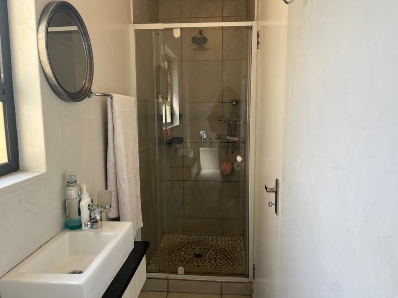 A compact bathroom featuring a tiled shower enclosure with a pebble-style floor and a modern wall-mounted basin.