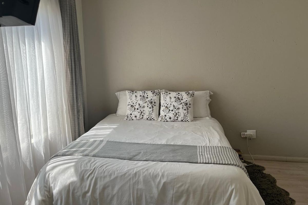 A cozy bedroom featuring neutral wall tones, natural light from the window, and standard electrical fixtures.