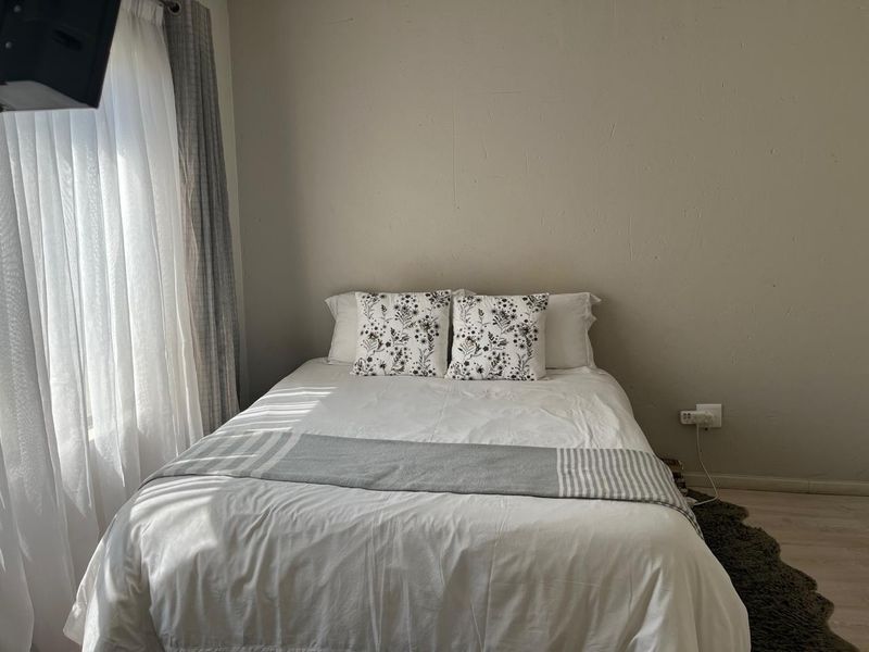 A cozy bedroom featuring neutral wall tones, natural light from the window, and standard electrical fixtures.