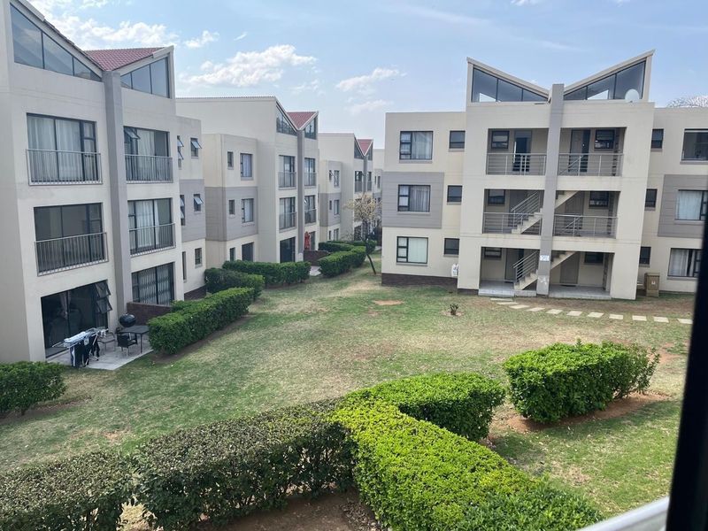 A view of the apartment complex exterior featuring landscaped gardens, paved walkways, and multi-story residential buildings with balconies.