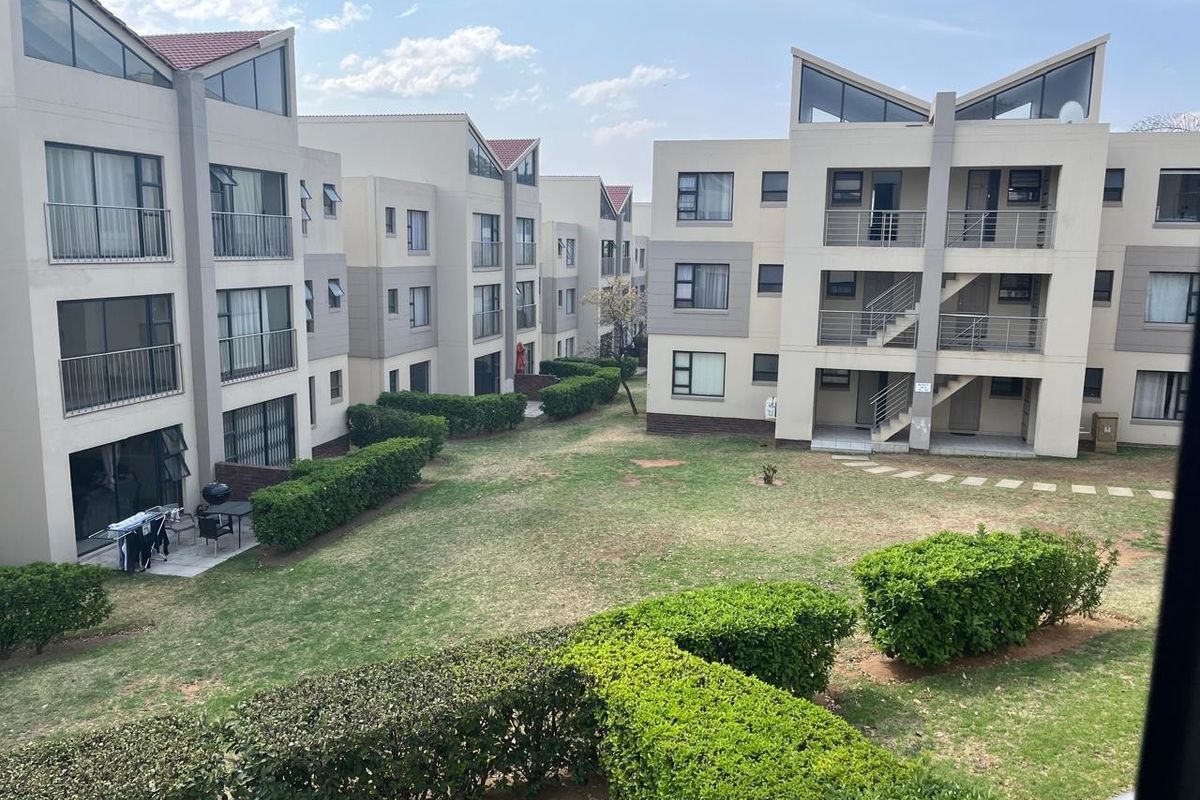A view of the apartment complex exterior featuring landscaped gardens, paved walkways, and multi-story residential buildings with balconies.