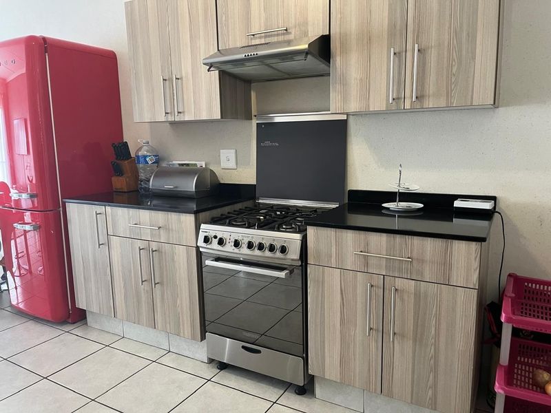 A functional kitchen featuring wood-grain cabinetry, black granite countertops, and a stainless steel gas stove with an integrated extractor fan.