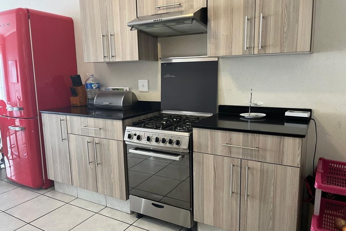 A functional kitchen featuring wood-grain cabinetry, black granite countertops, and a stainless steel gas stove with an integrated extractor fan.