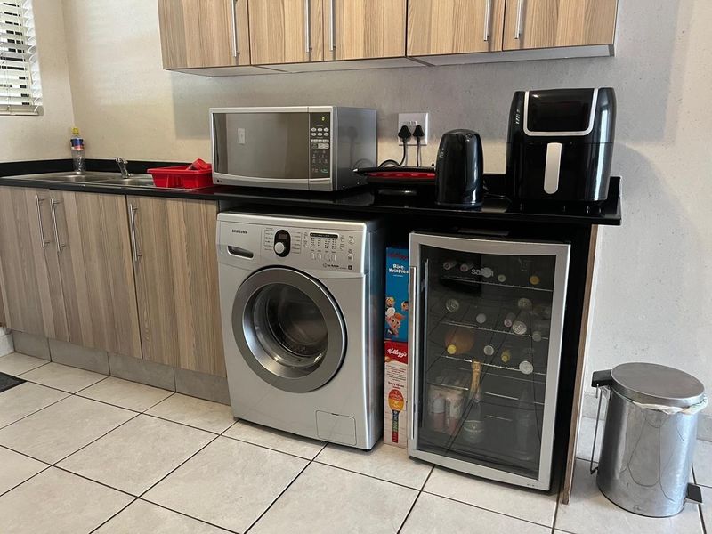 A functional laundry area featuring laminate cabinetry, black granite countertops, a stainless steel sink, and tiled flooring with integrated appliance space.