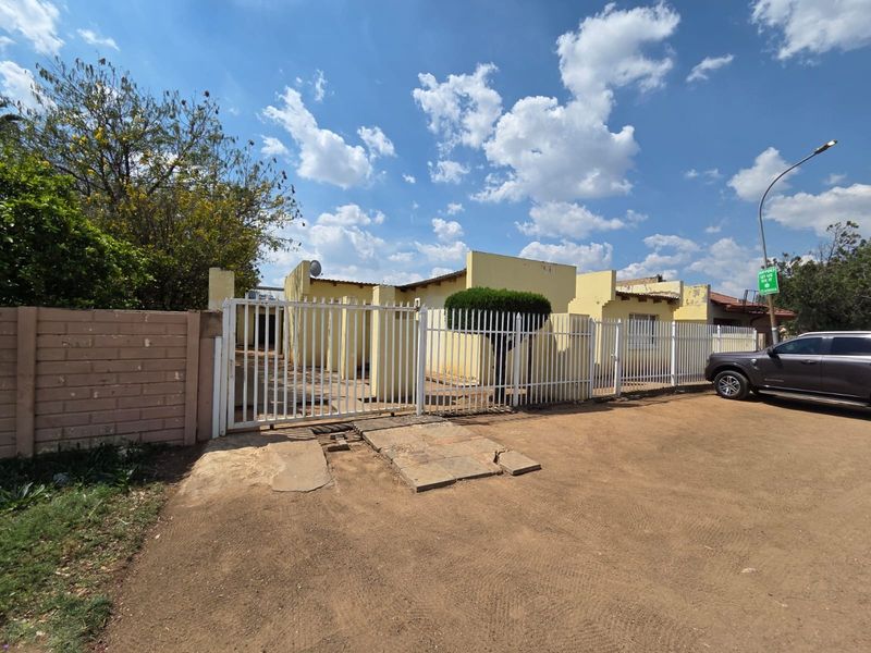 Front exterior view of the property featuring a metal security gate, perimeter wall, and a concrete driveway entrance.