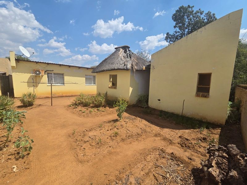 Rear view of the property showing multiple structures, including a thatched roof building requiring maintenance and a large garden area.