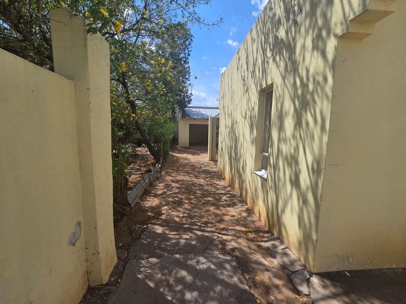 A side pathway leading to the rear of the property, featuring a concrete walkway, boundary wall, and access to a detached garage.
