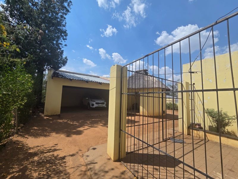 Front exterior view showing a gated entrance, open garage, and a small thatched structure with visible wear on the exterior wall finishes.