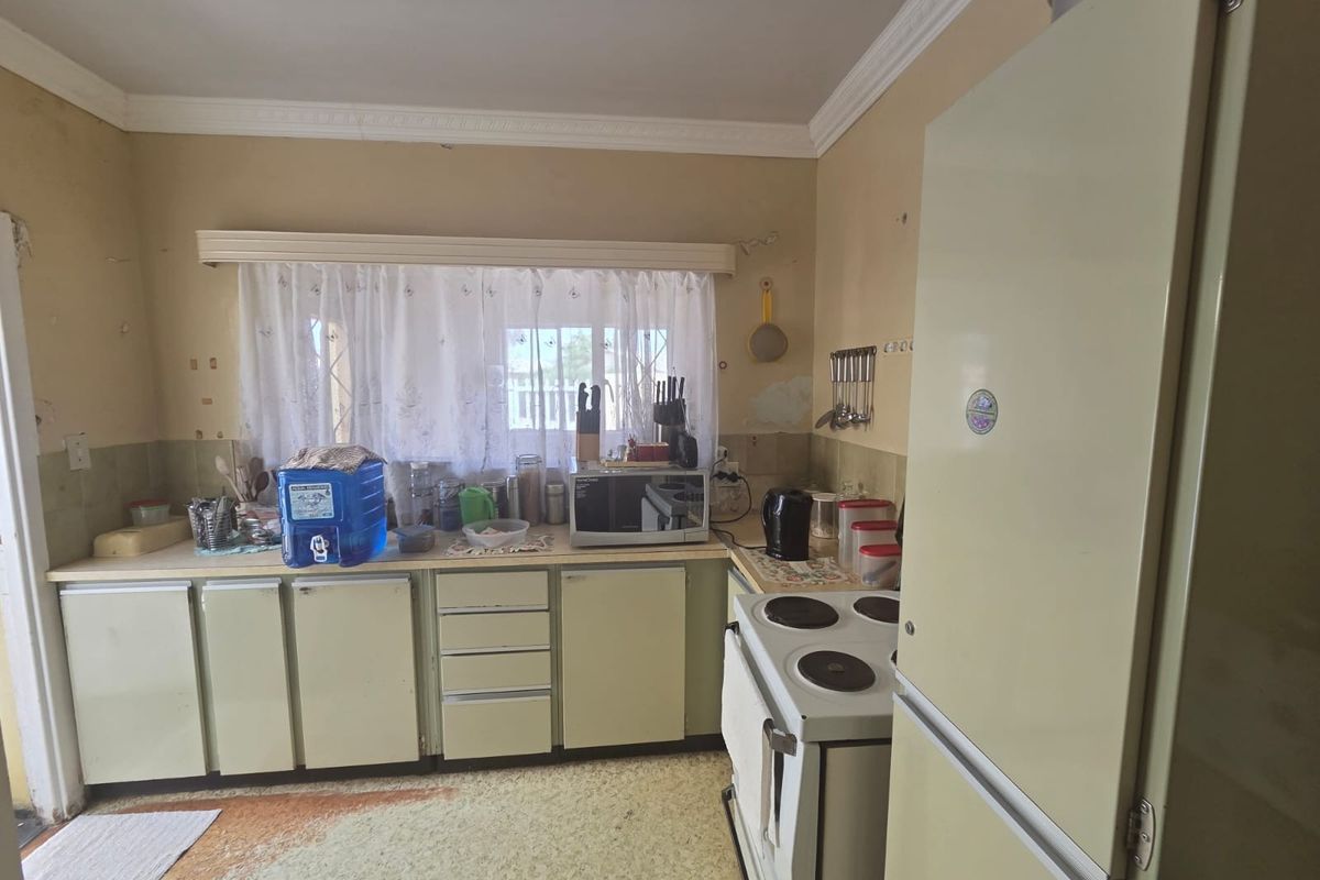 A dated kitchen featuring original cabinetry, laminate countertops, and an electric stove, requiring cosmetic updates and renovation to modernize the space.