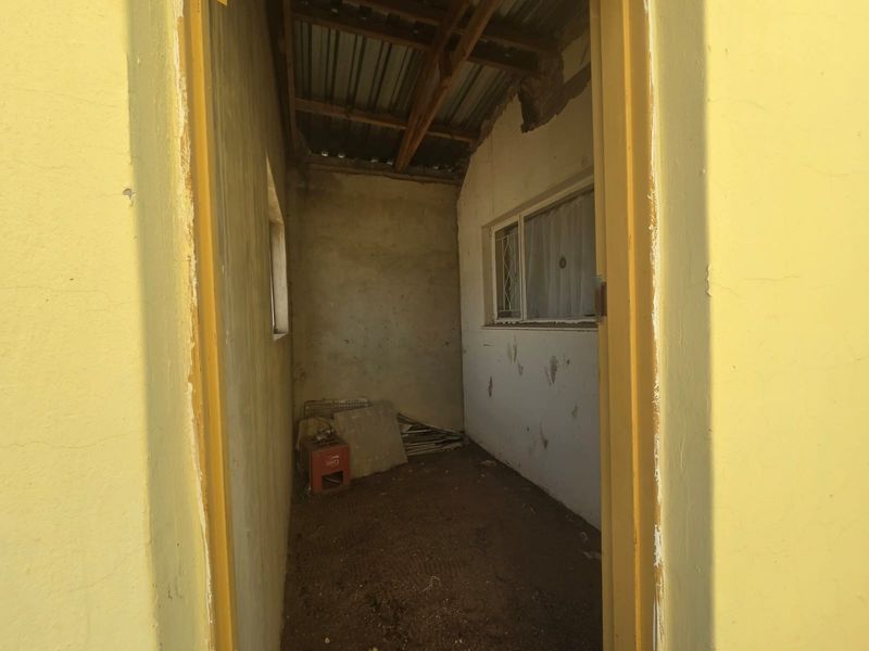A small, unfinished utility space featuring exposed timber roof beams, corrugated metal roofing, and basic wall finishes in need of significant repair and renovation.