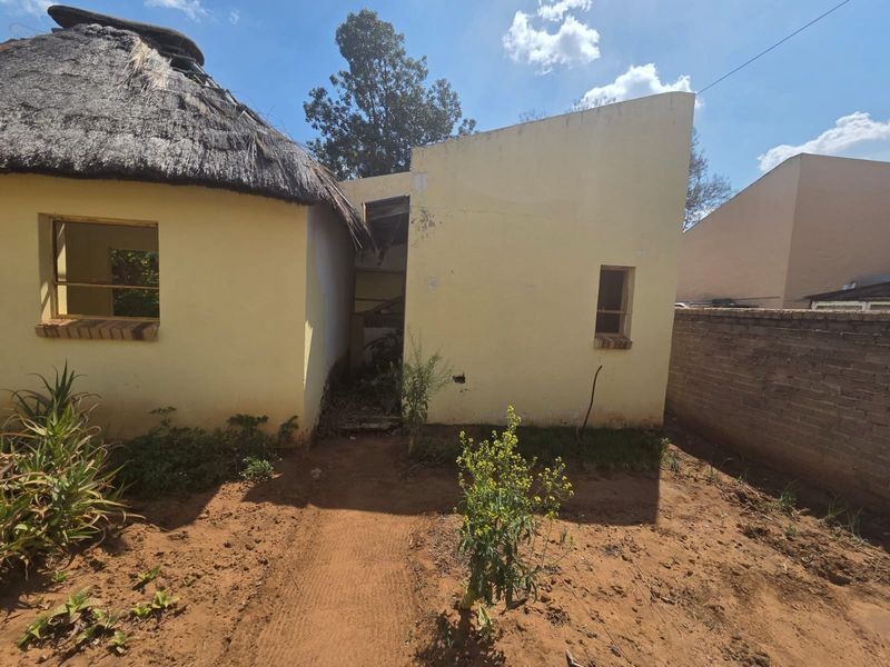 Rear view of a property featuring a thatched roof structure and masonry walls showing significant signs of wear and structural deterioration.