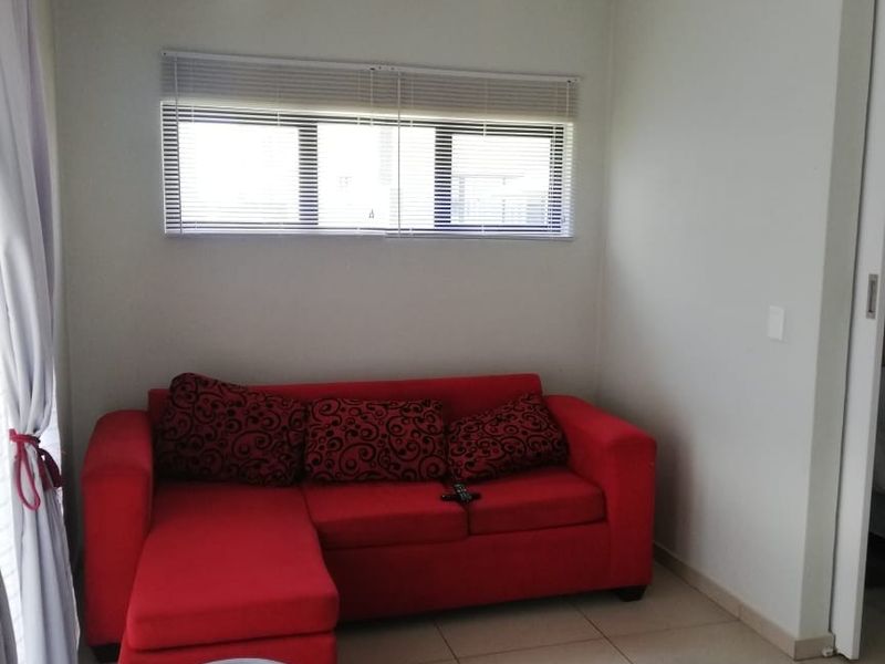 A compact living room featuring neutral tiled flooring, a window with venetian blinds, and access to an adjacent area via a sliding door.