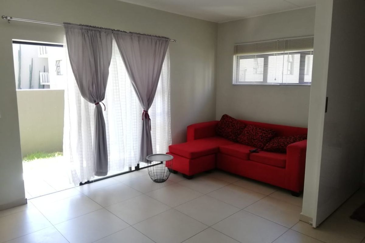 A bright living room featuring neutral tiled flooring, a sliding glass door leading to an outdoor area, and fitted window blinds.