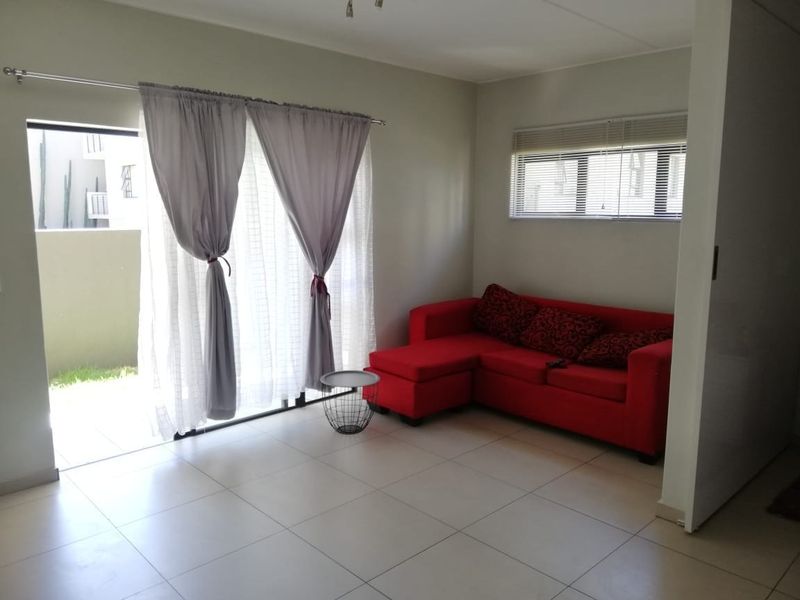 A bright living room featuring neutral tiled flooring, a sliding glass door leading to an outdoor area, and fitted window blinds.