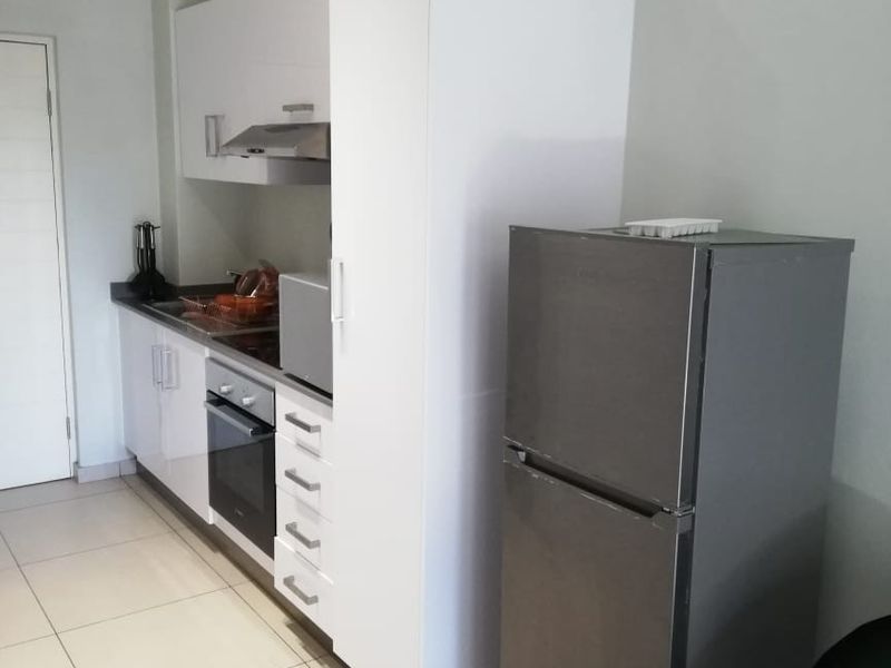 Modern kitchen featuring white built-in cabinetry, integrated oven and hob, extractor fan, and light-colored tiled flooring.