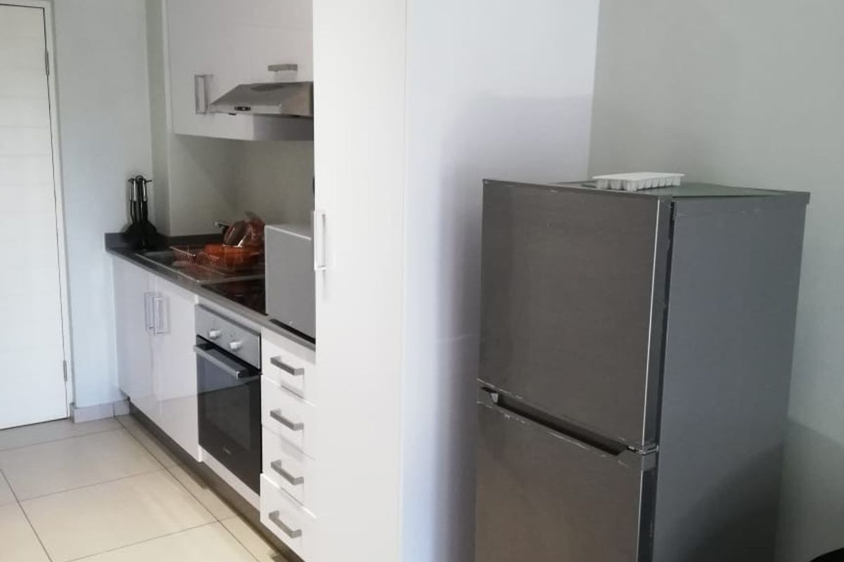 Modern kitchen featuring white built-in cabinetry, integrated oven and hob, extractor fan, and light-colored tiled flooring.