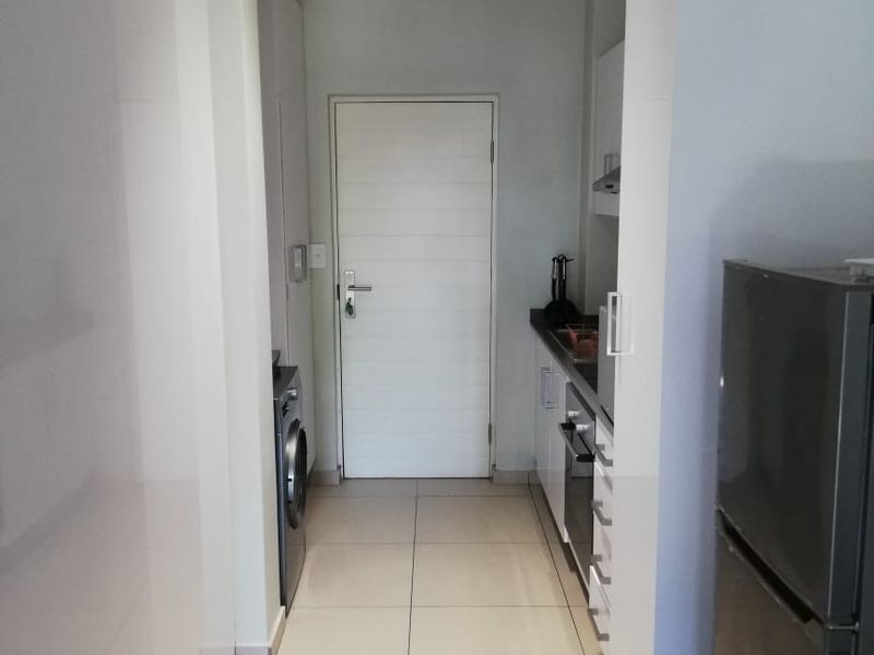 A compact, modern kitchen featuring sleek white cabinetry, tiled flooring, and integrated appliances, providing a functional and efficient workspace.